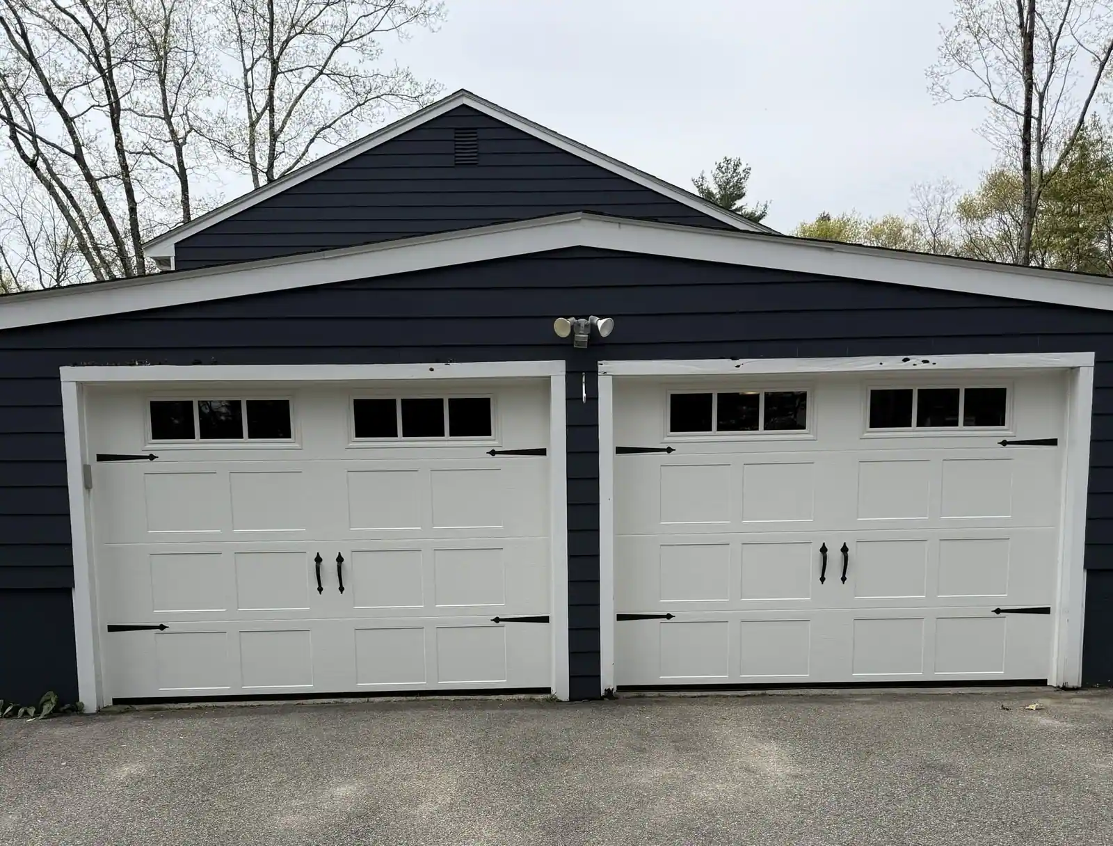 White carriage-style doors with black hardware on a deep blue house
